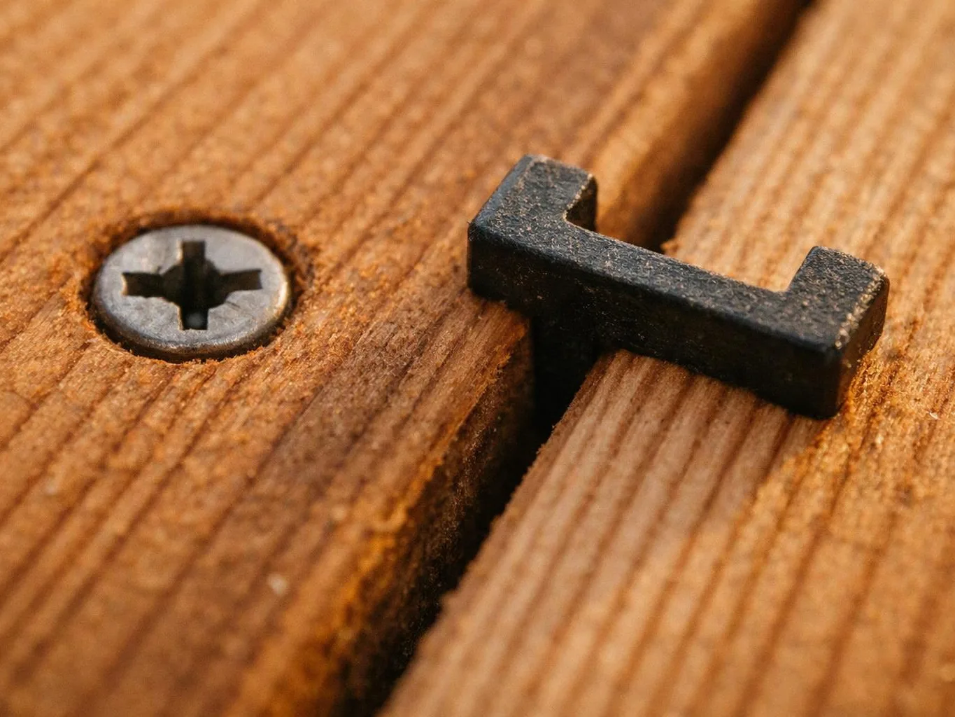 Close-up of a black metal fastener beside a screw on a wooden surface