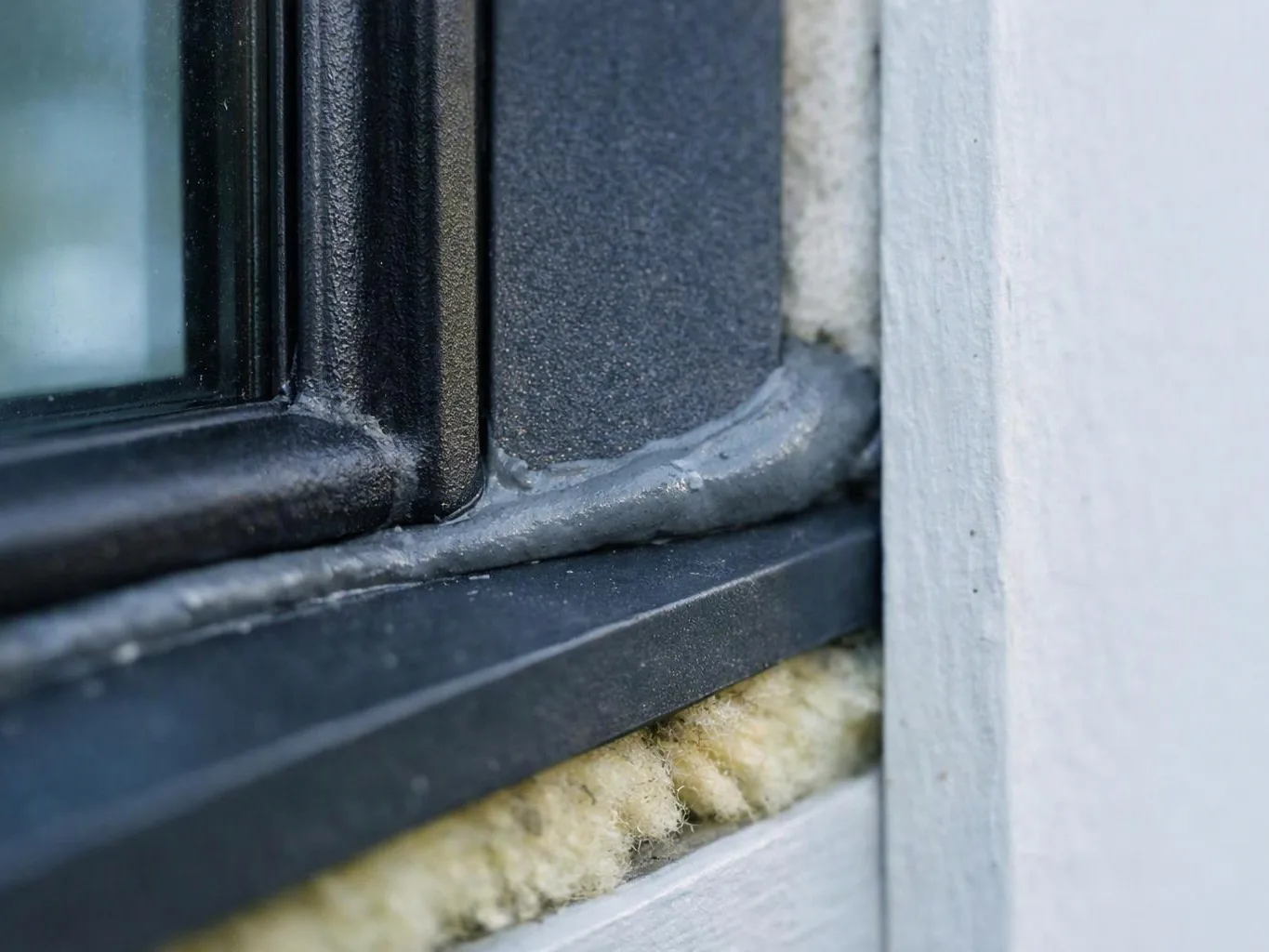 Close-up of a black window frame sealed against white siding with exposed insulation underneath