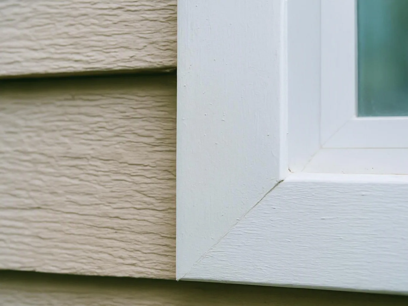 Close-up of a white window frame beside beige siding on a house exterior