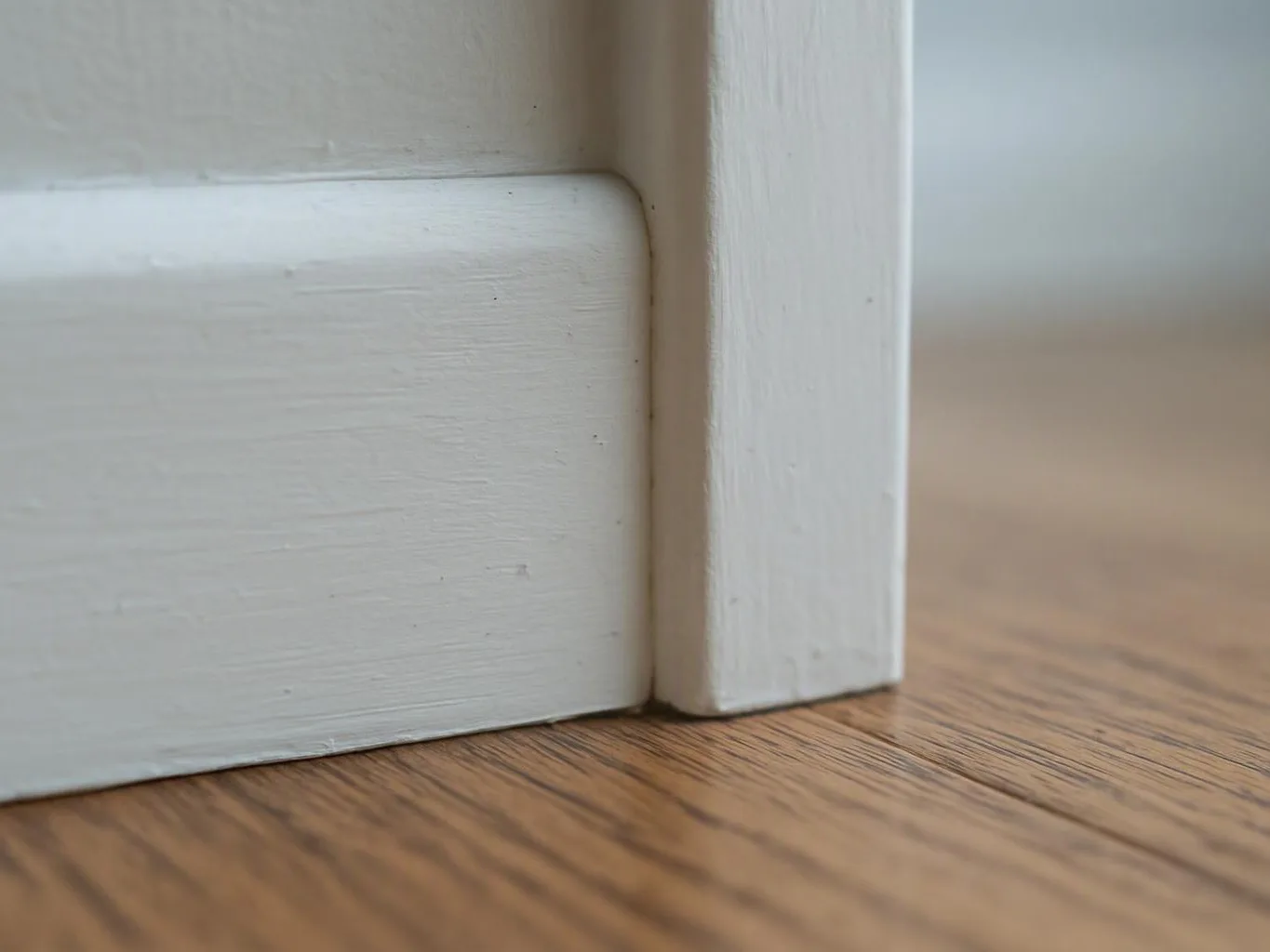 Close-up of a white wooden frame meeting a wood floor, showing the corner and grain texture