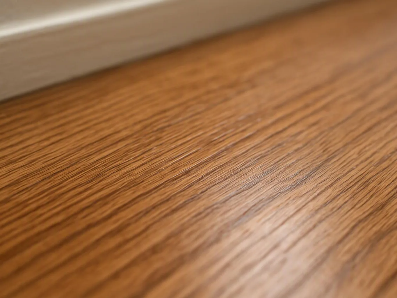 Close-up of a wood floor with warm grain and a blurred baseboard along the top edge