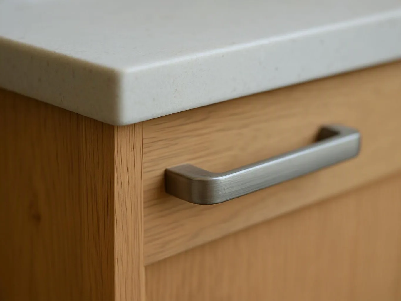 Close-up of a wooden cabinet drawer with a brushed metal handle beneath a light stone countertop